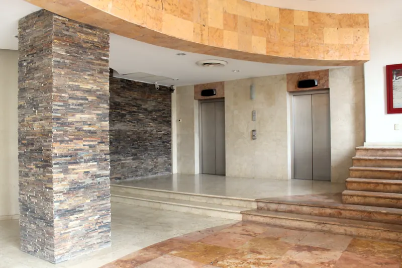 Vestíbulo del edificio con elevadores y muro de piedra