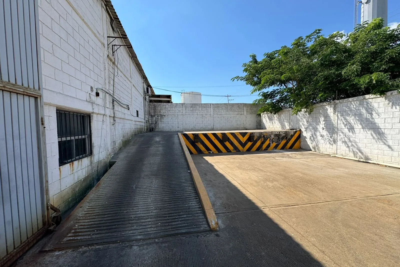 Andén de carga exterior con rampa de acceso y tope señalizado, junto al patio de maniobras